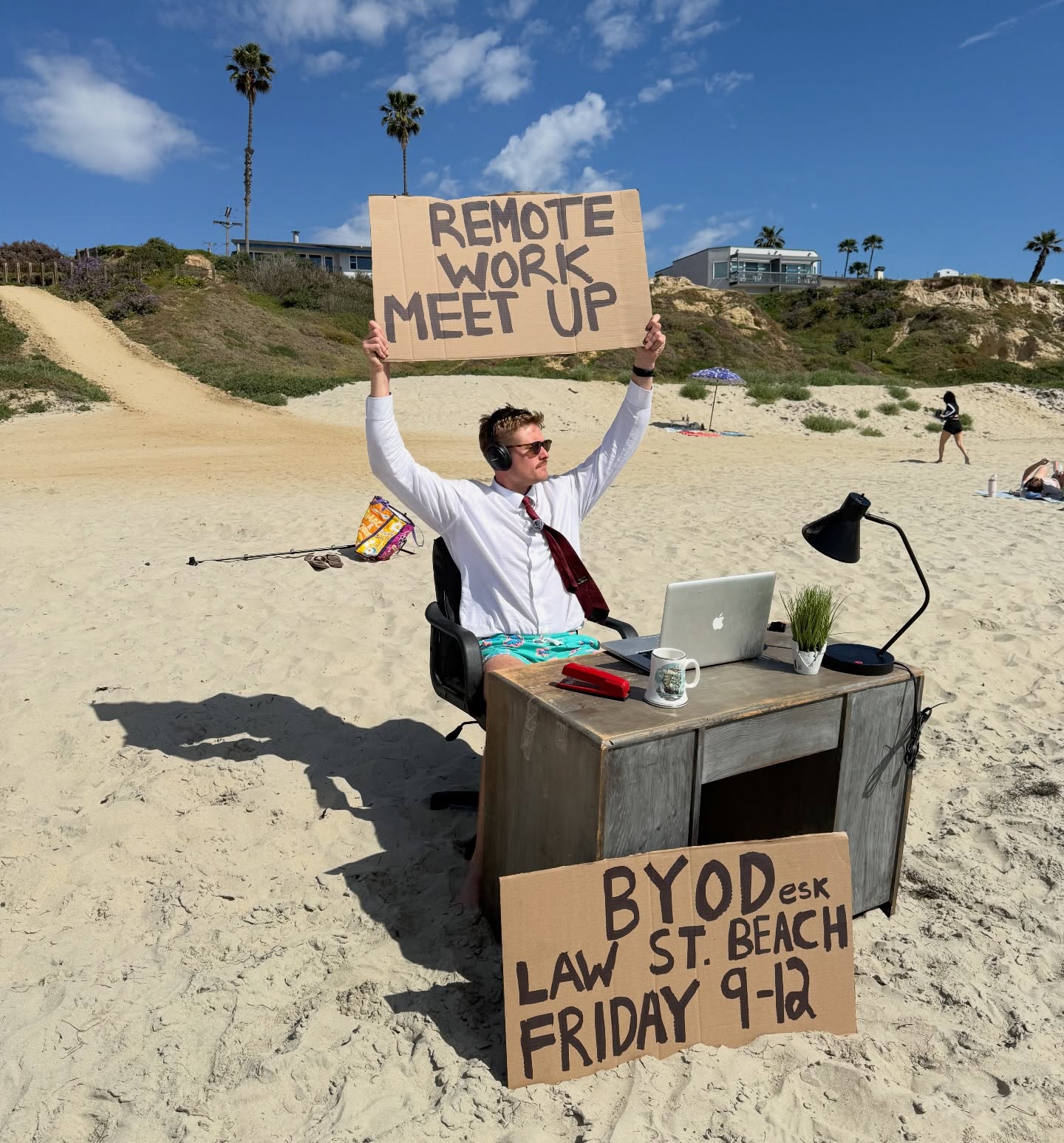 Scotty at his desk on Law Street Beach holding a Remote Work Meet Up sign